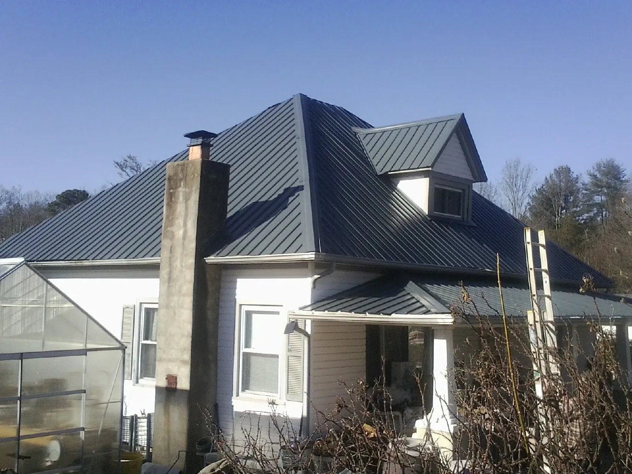 Dark blue standing seam metal roof on a white farmhouse with dormer in Covington
