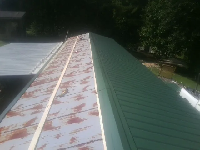 Old rusted panels beside newly installed green metal roofing — Wind Damage Roof Repair by Roofing Brothers in Covington